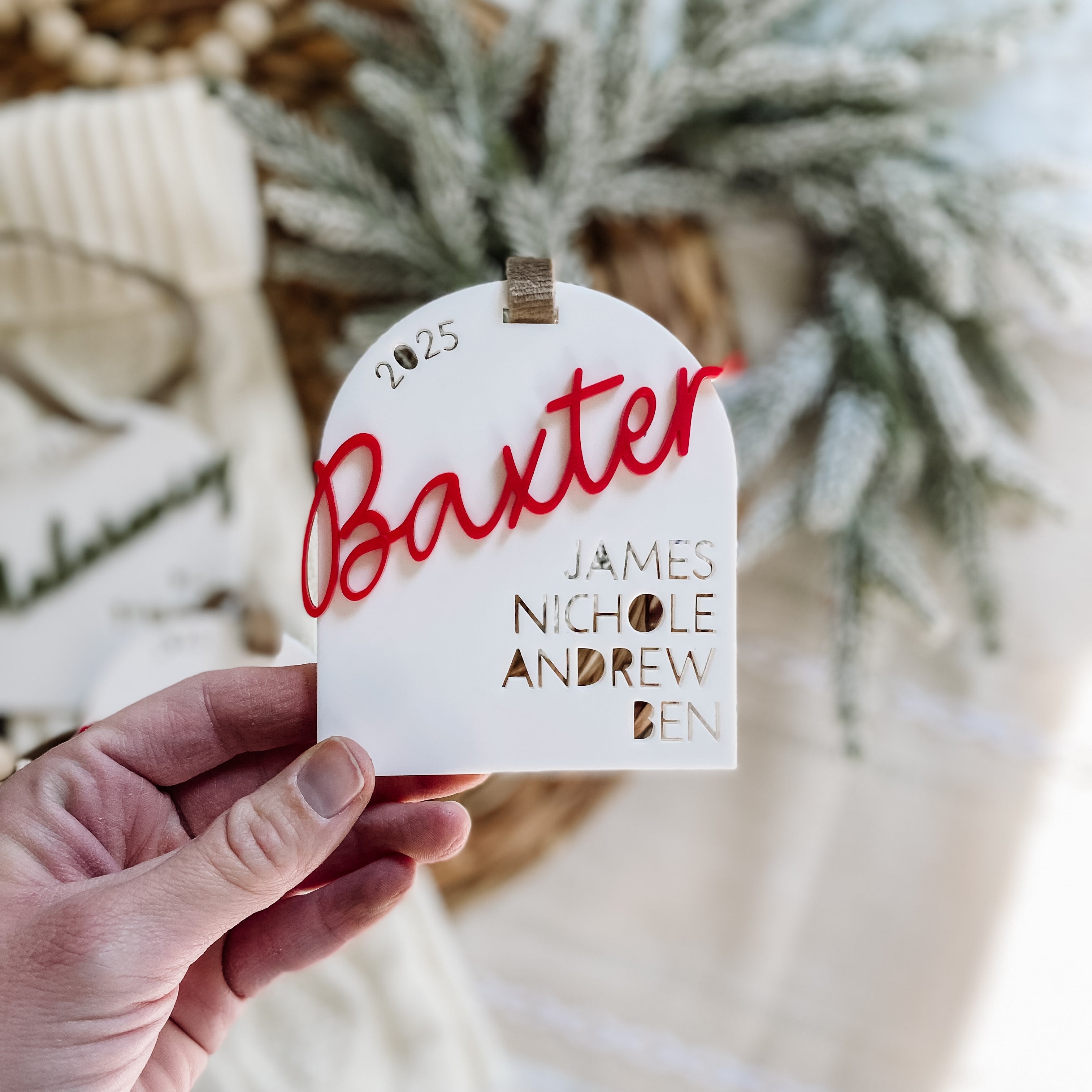 Personalized baby name ornament with 'Baxter' in red script, 2025, and family names, perfect for holiday decor.