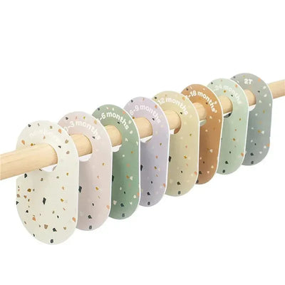 Colorful baby closet dividers labeled by age, ranging from newborn to 2T, displayed on a wooden rod.
