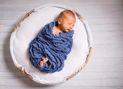 Sleeping newborn baby wrapped in a blue knit swaddle in a woven basket