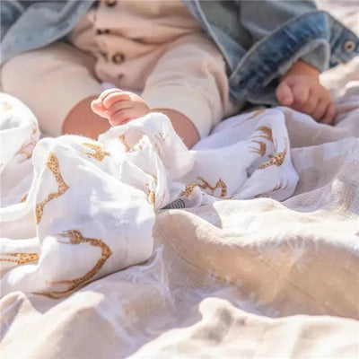 Aden + Anais Safari Dreams swaddle blanket with a baby’s feet peeking out, featuring animal prints in soft organic cotton.