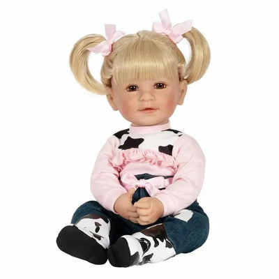Adora Doll, I Love Moo, features a toddler with blonde pigtails, wearing a pink cow-patterned top and blue jeans.