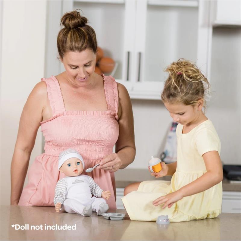 A woman and a girl play with a doll accessory set; the woman feeds a toy doll while the girl holds a feeding bottle.
