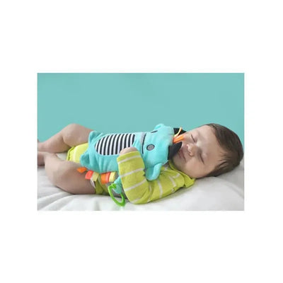 Baby sleeping on a white surface, cuddling a blue gripe belt with colorful attachments.