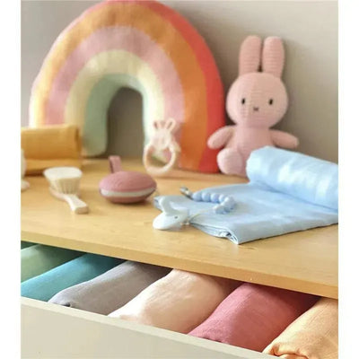 Ali + Oli Muslin Swaddle Blanket in taupe displayed among various baby items, including toys and colorful swaddles in a drawer.