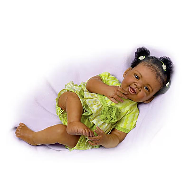 Realistic Ashton Drake Alexis Baby Doll wearing a green dress with a flower, lying on a light purple surface, smiling.