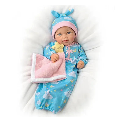Ashton Drake baby doll Rylee, dressed in a blue pajamas with a pink blanket and a star, cuddling a pink cloth.