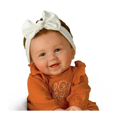 Lilah Baby Girl doll from Ashton Drake, featuring a smiling face, brown curly hair, and a white bow headband.
