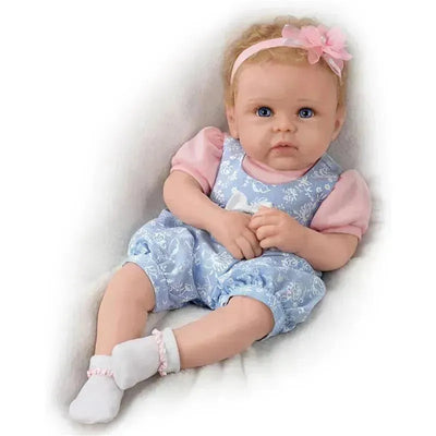 Silicone doll named Little Livie by Ashton Drake, featuring blue outfit, pink sleeves, and a flower headband.