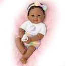 Ashton Drake Ciara baby doll with curly hair, wearing a unicorn-themed shirt and pastel shorts, holding a pacifier.