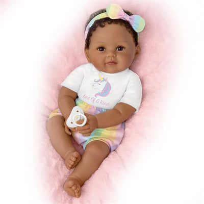 Ashton Drake Ciara baby doll with curly hair, wearing a unicorn-themed shirt and pastel shorts, holding a pacifier.