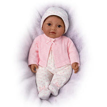 Lifelike toy doll named Little Kiara wearing a pink polka dot jacket and white outfit with pink hearts, resting on a soft blanket.