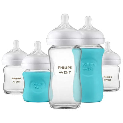 Avent Glass Natural Bottle Baby Set featuring four clear glass bottles with white caps and blue silicone sleeves.