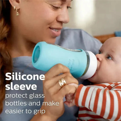 A mother feeds a baby with an Avent glass bottle featuring a silicone sleeve for grip and protection.