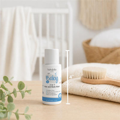 Travel size 2oz Baby Jolie 2-in-1 Hair and Body Wash with a white bottle displayed on a wooden surface next to a wooden brush and fabric.