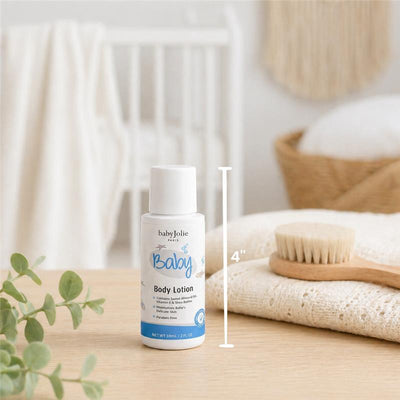 Baby Jolie body lotion, 2oz, displayed next to a wooden brush on a softly textured cloth, with a crib in the background.