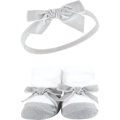 Black and silver headband with a bow above white socks adorned with gray bows in a gift set for baby girls.