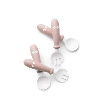 BabyBjorn baby spoon and fork set in powder pink, featuring rounded handles and playful face designs.