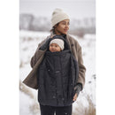 Winter cover for BabyBjörn carrier in black, worn by a woman holding a smiling baby, against a snowy backdrop.