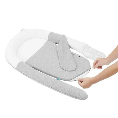 Organic grey Babymoov Cloudnest Soothing Lounger with a removable cover; hands adjusting the cover are visible.