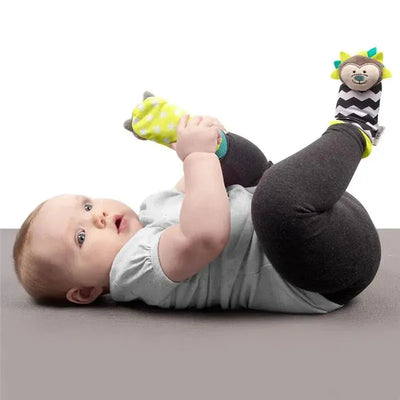 Infant lying on a gray surface wearing Bbluv Duo Foot Finders socks featuring a hedgehog and a racoon design.