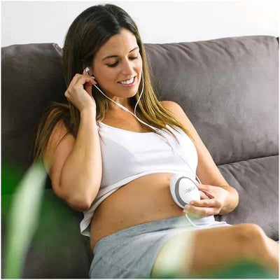 Woman using the Bbluv Echö Wireless Fetal Doppler on her pregnant belly, listening through earphones with a relaxed expression.