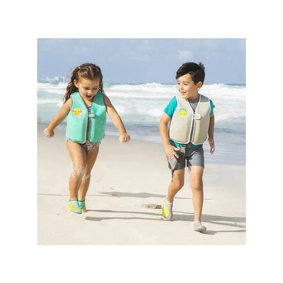 Two children, a girl in a light blue swim vest and a boy in a beige swim vest, play together on a sandy beach.