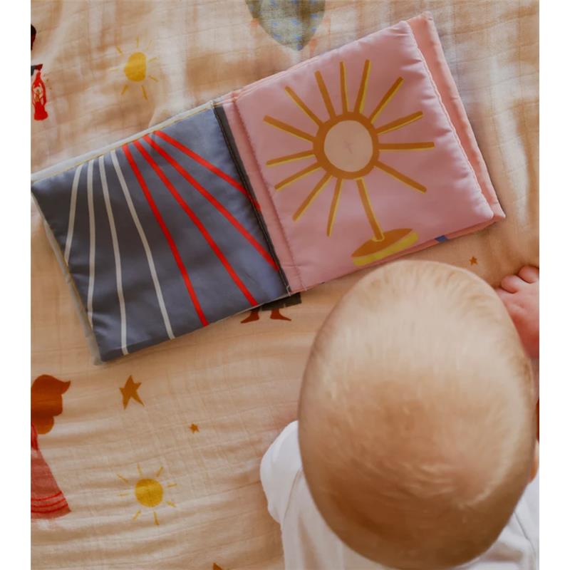 Soft fabric crinkle book featuring colorful designs, placed on a patterned surface with a baby observing it.