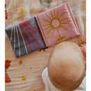 Soft fabric crinkle book featuring colorful designs, placed on a patterned surface with a baby observing it.