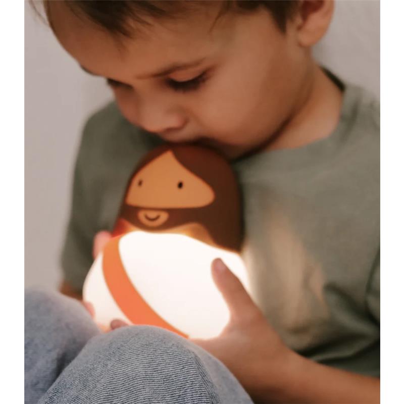 Child holds a glowing Jesus-shaped night light, gently kissing it, with a soft, comforting ambiance.