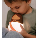 Child holds a glowing Jesus-shaped night light, gently kissing it, with a soft, comforting ambiance.