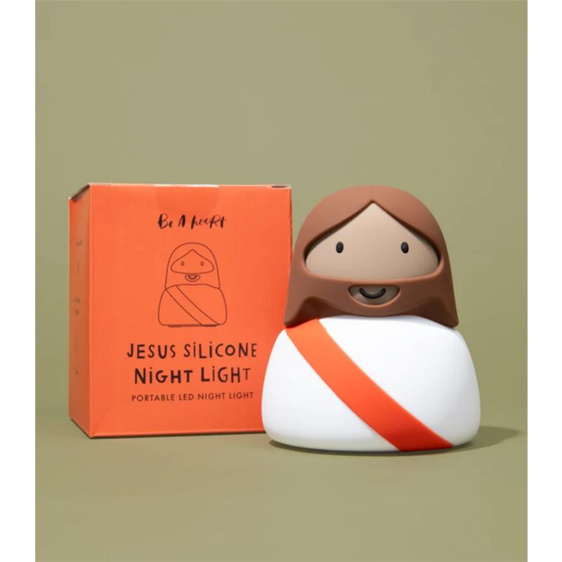 Jesus silicone night light with a smiling face and orange sash, next to its orange packaging, on a neutral background.