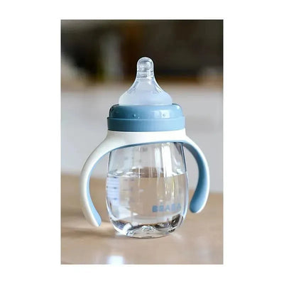 Beaba 2-in-1 Bottle to Sippy Learning Cup in Rain color, featuring handles and a clear design with water inside.