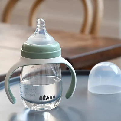 2-in-1 Beaba bottle to sippy training cup in sage color, featuring removable lid and handles, with clear liquid inside.