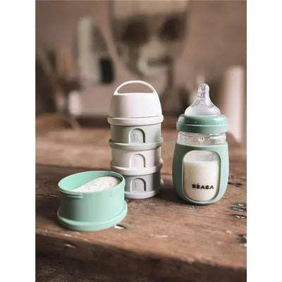 Beaba 2-In-1 Glass Training Cup in sage, accompanied by stackable storage containers and a small green bowl.
