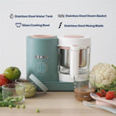 Beaba Babycook Neo, a baby food maker in cotton candy color, features a glass bowl and stainless steel components, with fresh vegetables nearby.