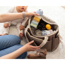 Translucent Beaba Formula Snack Container in pastel colors, held above a bag containing snacks and baby items near a baby and a dog.