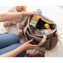 Translucent Beaba Formula Snack Container in pastel colors, held above a bag containing snacks and baby items near a baby and a dog.