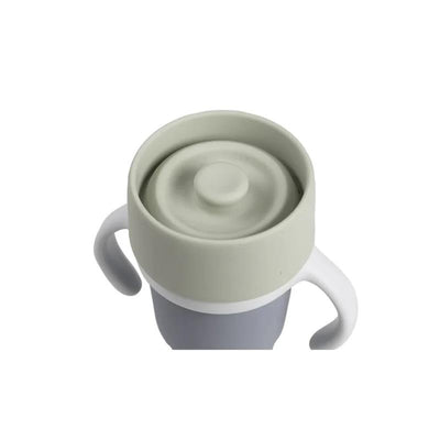 Beaba Stainless Steel 360 Learning Cup in Pebble color, featuring a grey body, soft green lid, and handles for easy grip.