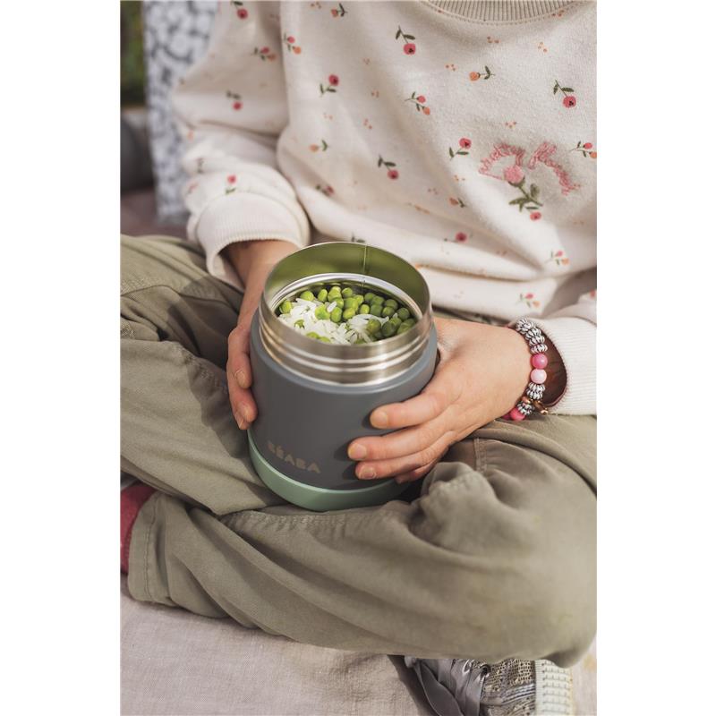 Beaba stainless steel insulated food jar in sage color held by a child, filled with green peas and rice.