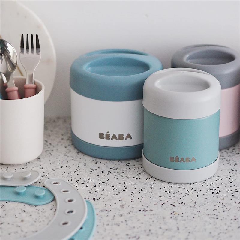Beaba Stainless Steel Insulated Food Jar in Sage color, 10 oz, displayed among utensils and other jars on a countertop.