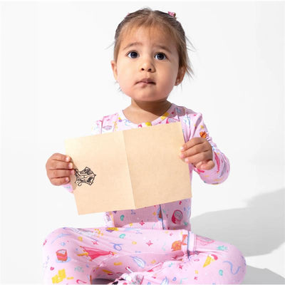 Toddler in pink pajamas holding a blank card with a Harry Potter emblem, looking attentively at the camera.
