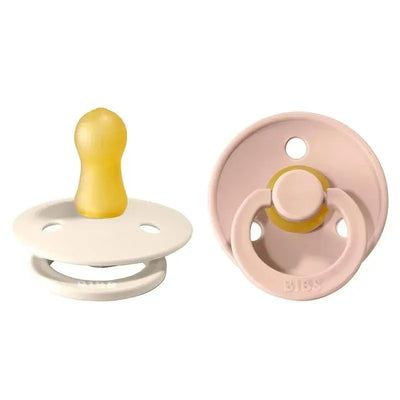 Blush and ivory natural rubber baby pacifiers, featuring a round shield, yellow nipple, and BIBS logo. Suitable for 0-6 months.