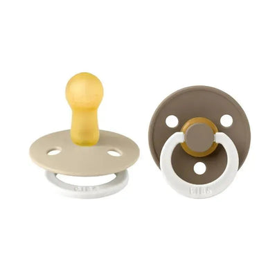 Two BIBS rubber baby pacifiers in Vanilla and Dark Oak shades, designed for ages 6 to 18 months.