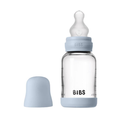 Silicone baby bottle in baby blue with a clear glass body, featuring a protective bumper and a nipple on top.