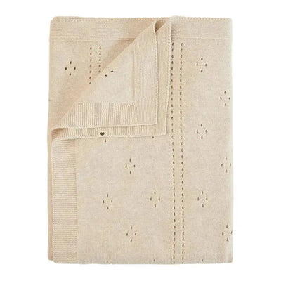 Knitted ivory blanket with an intricate pointelle pattern featuring small diamond shapes and a folded corner.