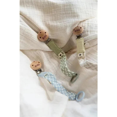 Bibs pacifier clips in petrol and baby blue, featuring wooden clips and fabric straps with patterns, on a soft background.
