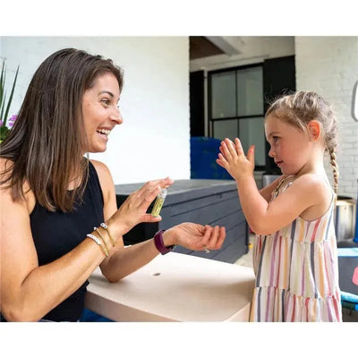 A woman demonstrates Boogie Wipes hand sanitizer spray to a young girl, who is clapping her hands excitedly.