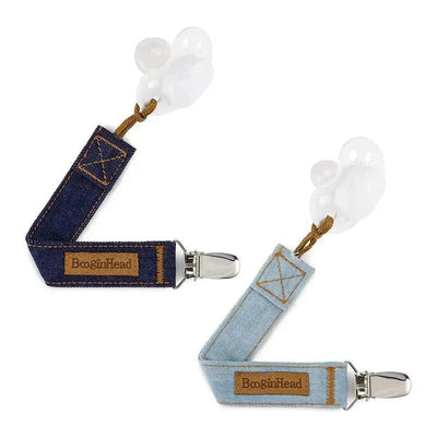 Two pacifier clips from BooginHead, one denim blue and one light denim, each featuring a clip and textured surface.