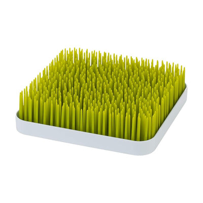 Green Boon Grass countertop drying rack for baby bottles and pacifiers, featuring tall, grass-like drying prongs on a square base.