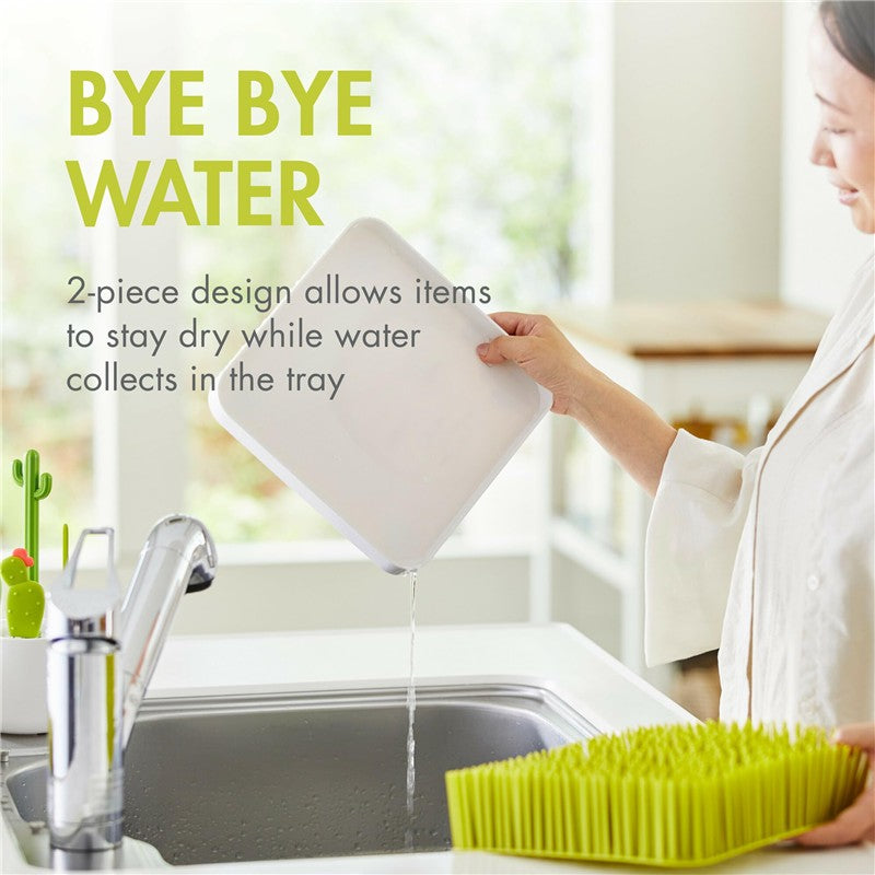 Green Boon Grass Countertop Drying Rack shown with a woman pouring water into a sink, highlighting its drying features.